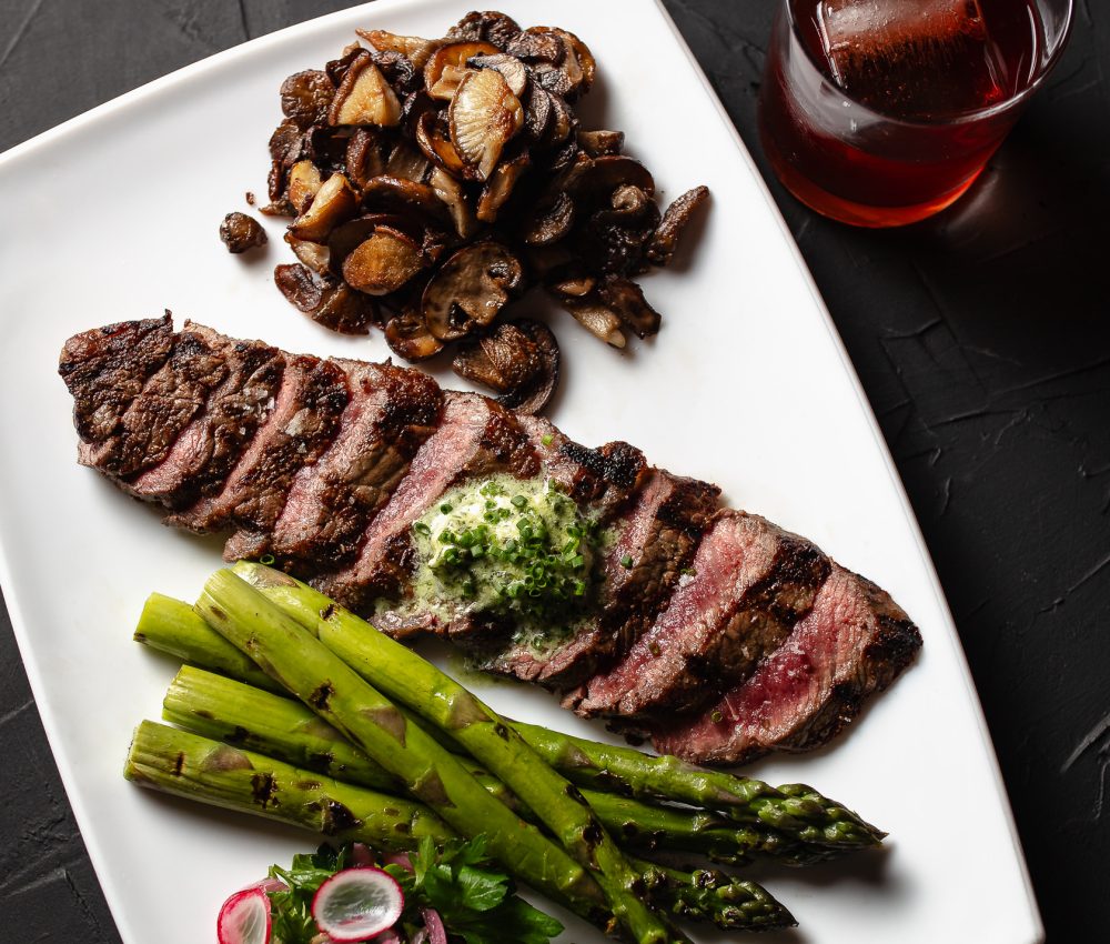 Australian Wagyu Strip with mushrooms and asparagus on a plate with a cocktail