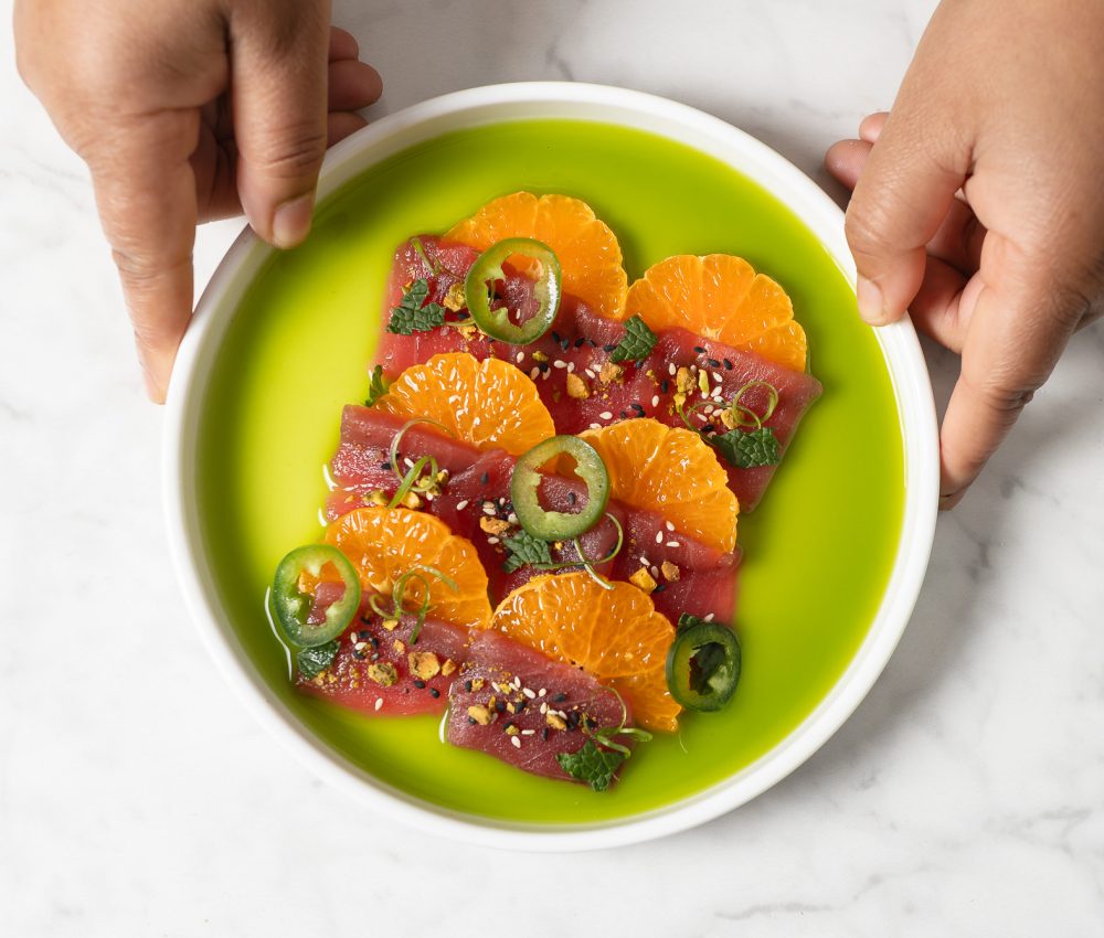 Chef's hands holding a dish of Clementine Tuna Crudo